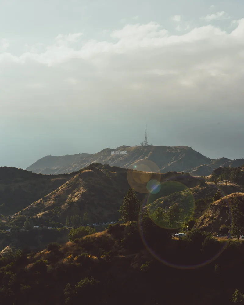 Sunlit hills below the Hollywood sign, with clouds and lens flare.